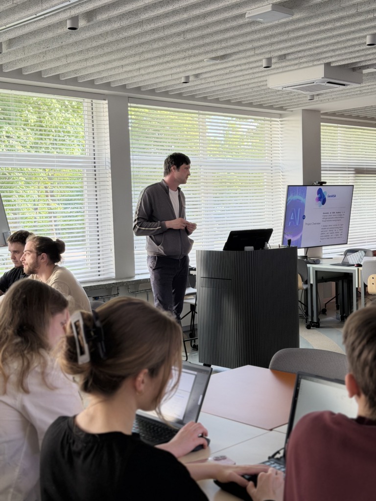 A presenter leads a classroom session while students work on laptops during the GenAISA Generative AI Skills Academy workshop. A large screen displays a project overview slide about generative AI skills in education.